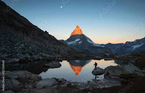 Hiker on a rock in the Riffelsee watching the first sunlight on the Matterhorn.