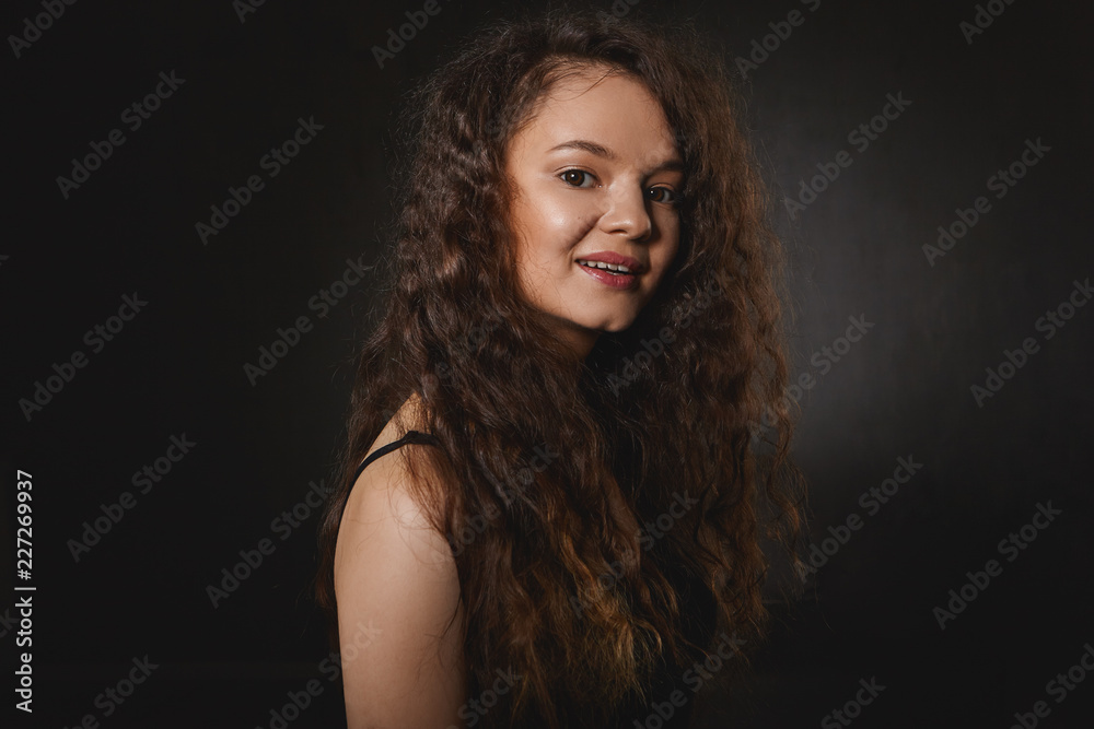 People, beauty, style and fashion concept. Amazing cute young brunette female model with long curly hair posing isolated at black studio wall, advertising shampoo and other hair care products People, beauty, style and fashion concept. Amazing cute young brunette female model with long curly hair posing isolated at black studio wall, advertising shampoo and other hair care products