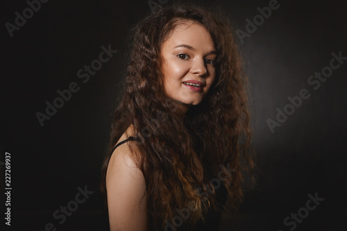 People, beauty, style and fashion concept. Amazing cute young brunette female model with long curly hair posing isolated at black studio wall, advertising shampoo and other hair care products