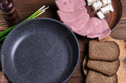 Empty pan for text and ingredients for a wholesome breakfast or lunch. Ham  feta cheese and pieces of bread on a brown wooden table.