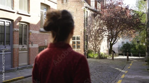 Spring sunny day in european city. Following from behind young woman walking between brick walls. Buildings in traditional dutch style. Ghent, Belgium photo