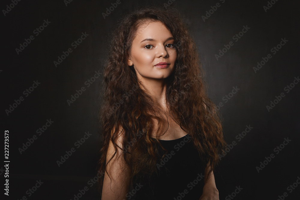 People, beauty and lifestyle concept. Isolated shot of mysterious young female with black eyes and voluminous dark hair looking at camera with smile. Charming brunette woman having pensive look People, beauty and lifestyle concept. Isolated shot of mysterious young female with black eyes and voluminous dark hair looking at camera with smile. Charming brunette woman having pensive look