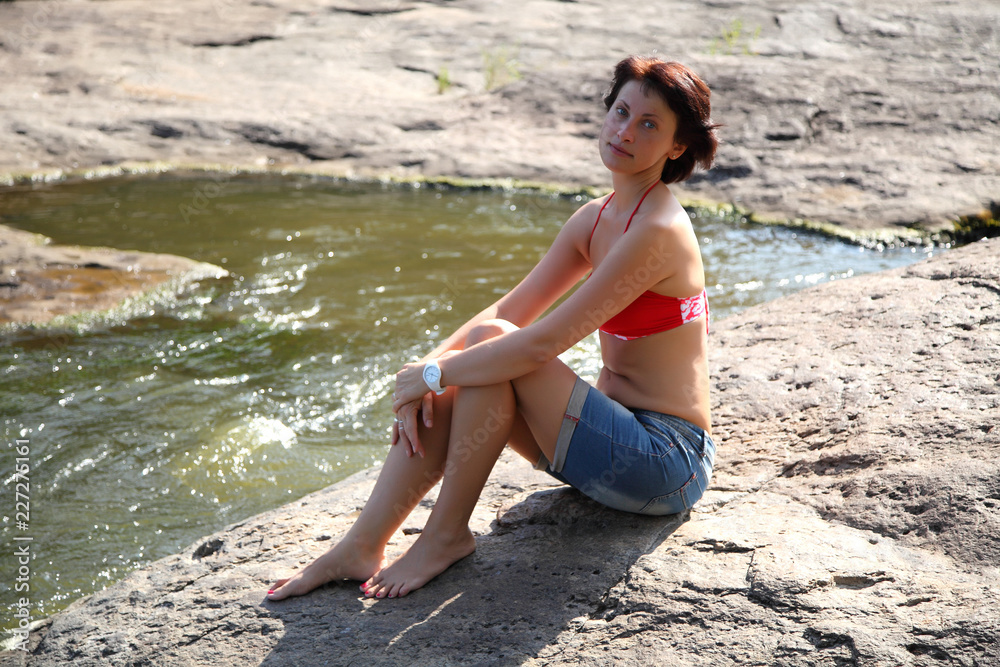 Woman on the beach by the lake. Beautiful young woman bathes in the rays of the summer sun on a hill above the river. Woman on the beach by the lake. Beautiful young woman bathes in the rays of the summer sun on a hill above the river.