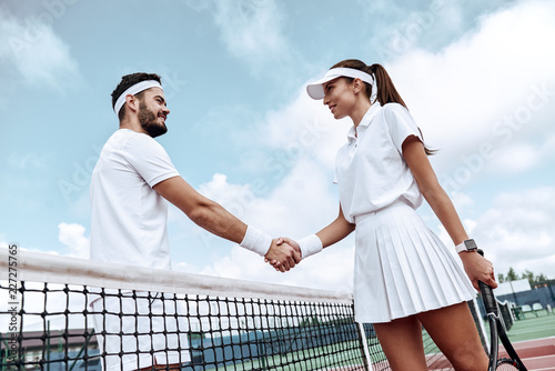 Shaking hands after good game. Man and woman in wristband shaking hands upon the tennis net © Friends Stock