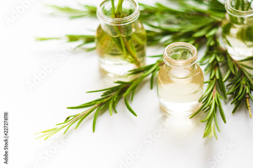 Rosemary essential oil in small bottles with a fresh rosemary twigs closeup, selective focus