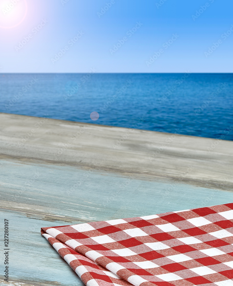 Empty weathered wooden table edge with checkered tablecloth with sea background Empty weathered wooden table edge with checkered tablecloth with sea background