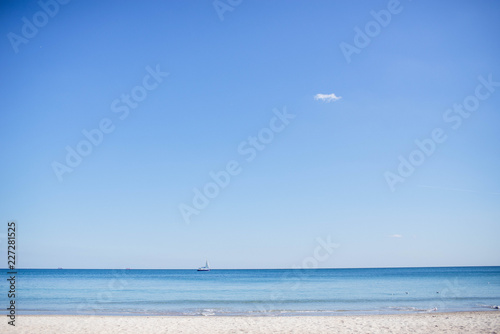 Sunny bright morning on a sandy beach near the blue sea, and also a white beautiful romantic sailboat on the horizon of a clear sky