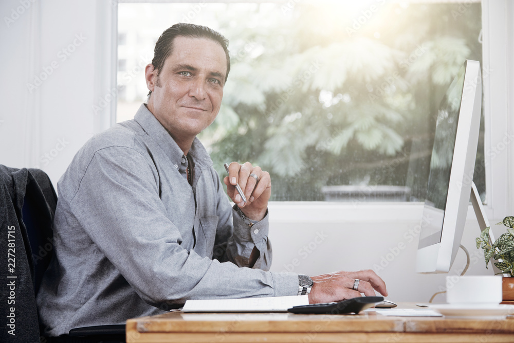 Portrait of mature businessman sitting in front of big computer screen at modern office Portrait of mature businessman sitting in front of big computer screen at modern office