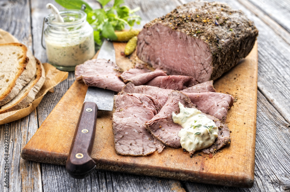 Traditional lunch meat with sliced cold cuts roast beef, remoulade and farmhouse bread as closeup on a cutting board