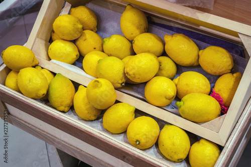 Shelf with a fresh yellow lemons in the crate. Choosing fruit  from the wooden box in the bio supermarket or grocery store, farm market.
