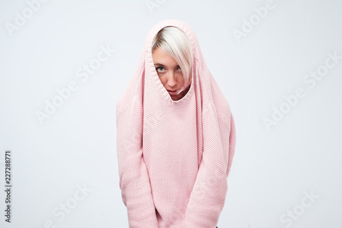 A pretty caucasian girl with a social phobia hides her face in a sweater.