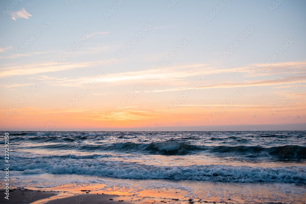 Sunrise and a beautiful cloudy sky early in the morning on the sandy shore on which the sea water beats and turns into foam Sunrise and a beautiful cloudy sky early in the morning on the sandy shore on which the sea water beats and turns into foam