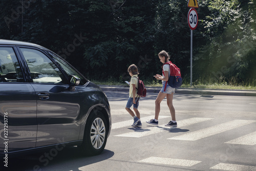 Fototapeta Car in front of children on pedestrian crossing walking from the school and look