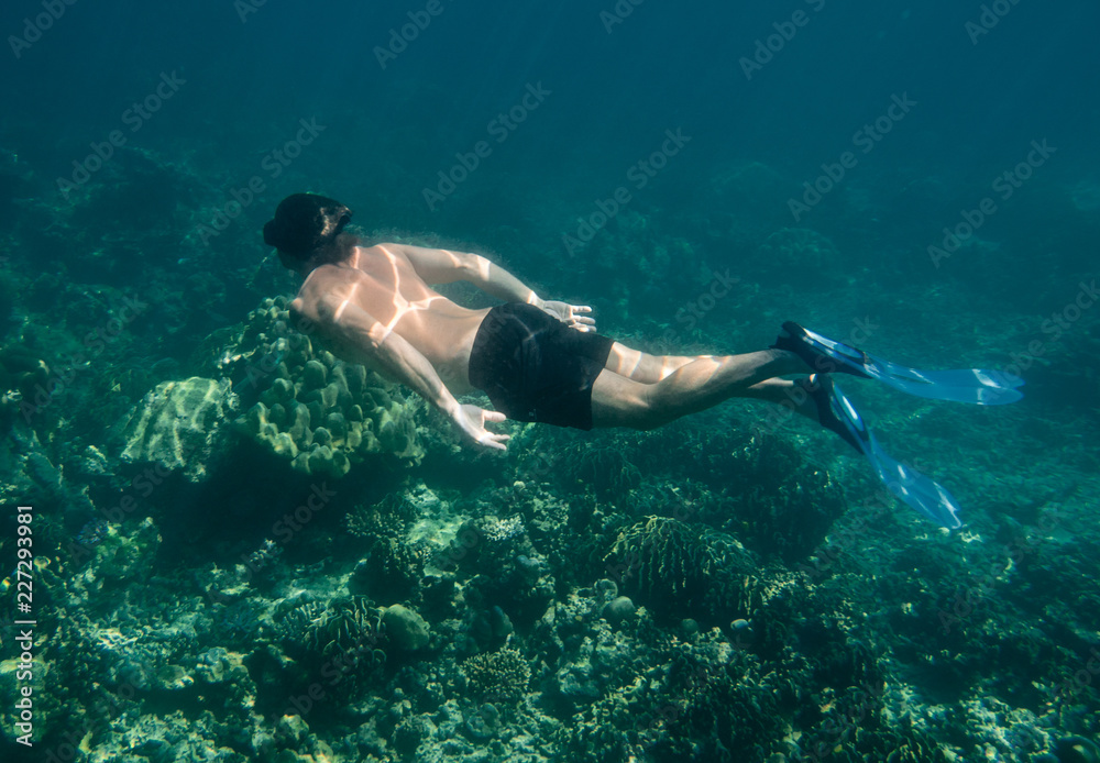 Man in flippers snorkeling underwater above the coral reefs in blue ocean depth