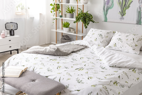Green plant pattern on white bedding and pillows on a bed in a nature loving bedroom interior. Real photo.