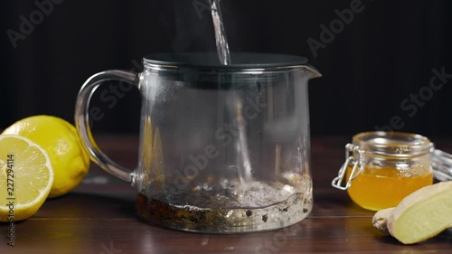 Boiling water is poured to the teapot with black tea, vitamin tea with lemon, ginger and honey, drink against sickness, hot drink photo