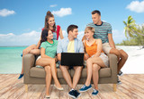friendship, leisure and technology concept - group of happy smiling friends with laptop computer sitting on sofa over tropical beach background in french polynesia