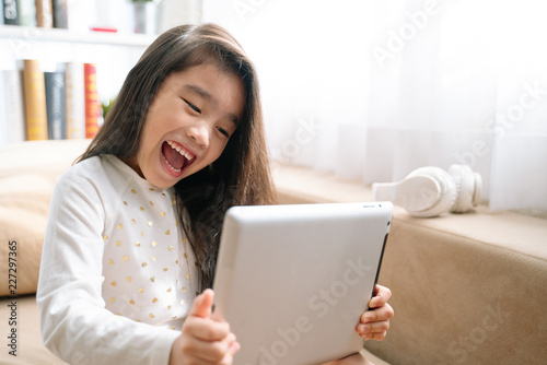 Asian Cute child playing games with a tablet and smiling while sitting on sofa at home