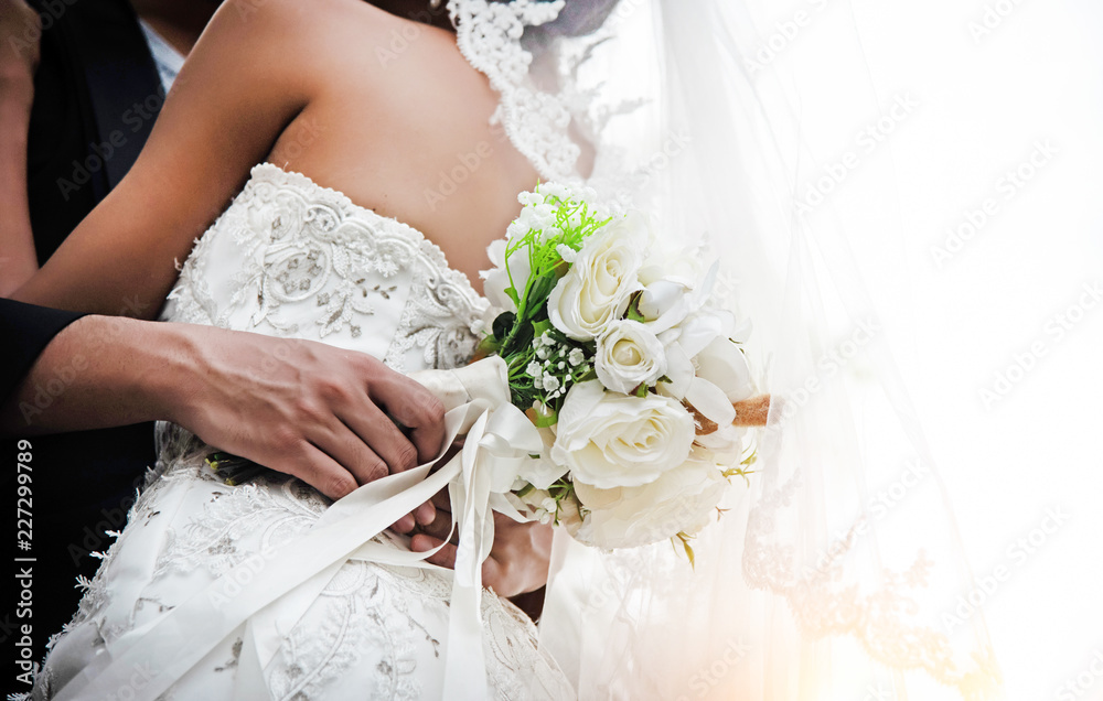 Naklejka premium The wedding couple.Bride and groom holding together,with white rose bouquet in hand,blurry lightaround