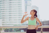 Beautiful fitness athlete woman drinking water after work out exercising on sunset evening summer in city outdoor portrait.Young woman drinking water after jogging