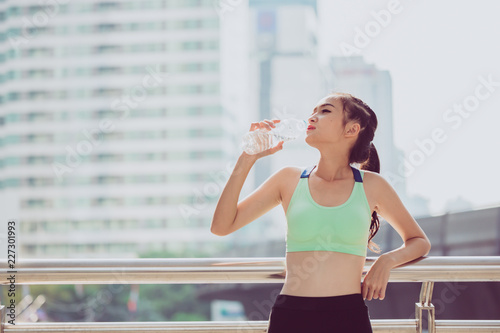 Beautiful fitness athlete woman drinking water after work out exercising on sunset evening summer in city outdoor portrait.Young woman drinking water after jogging © Yingyaipumi