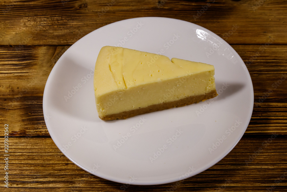 Piece of tasty sweet New York cheesecake in a white plate on wooden table