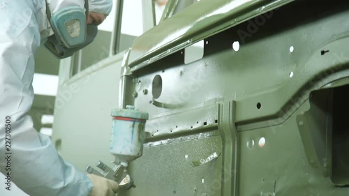 worker in respirator paints lorry cabin door with sprayer photo