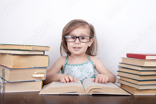 Beautiful little girl is sitting at the table with a bunch of books
