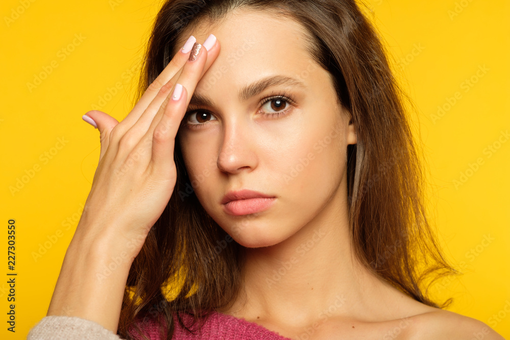 Fototapeta premium headache and migraine. fatigue and exhaustion. woman touching her forehead. pain meds or stress relieving techniques concept. young girl portrait on yellow background.