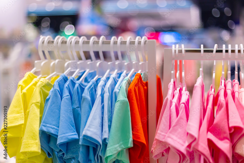 Colorful t-shirts children's wear on hang for sale in shop. Summer season children's clothes department store. Summer sale in shopping mall. Colorful t-shirts children's wear on hang for sale in shop. Summer season children's clothes department store. Summer sale in shopping mall.
