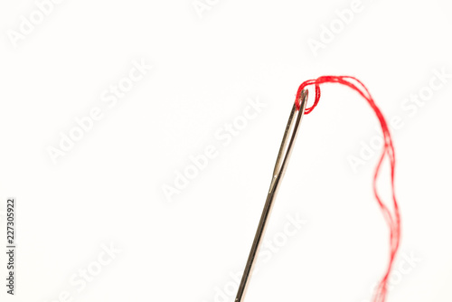Needle with eye red thread close up macro shot isolated on white background,