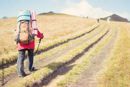 Woman with a large backpack with walking sticks in a hike in the mountains.