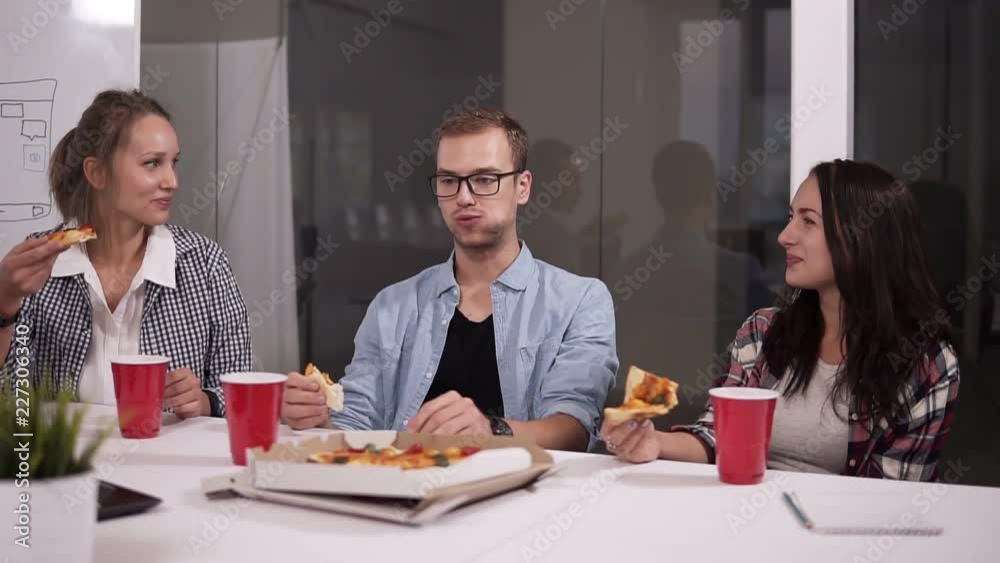 Young caucasian coworkers having lunch break eating pizza together in office. Laughing, talking, having fun. Food, business lunch and people concept - happy creative team eating pizza at office Young caucasian coworkers having lunch break eating pizza together in office. Laughing, talking, having fun. Food, business lunch and people concept - happy creative team eating pizza at office