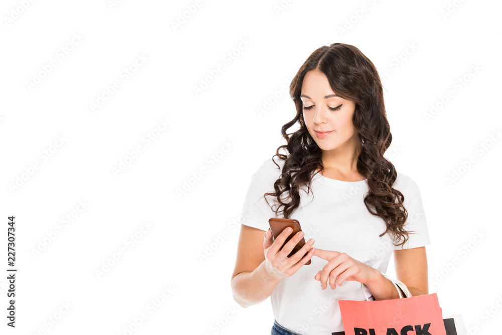 attractive shopper using smartphone and holding shopping bags with black friday sign isolated on white attractive shopper using smartphone and holding shopping bags with black friday sign isolated on white