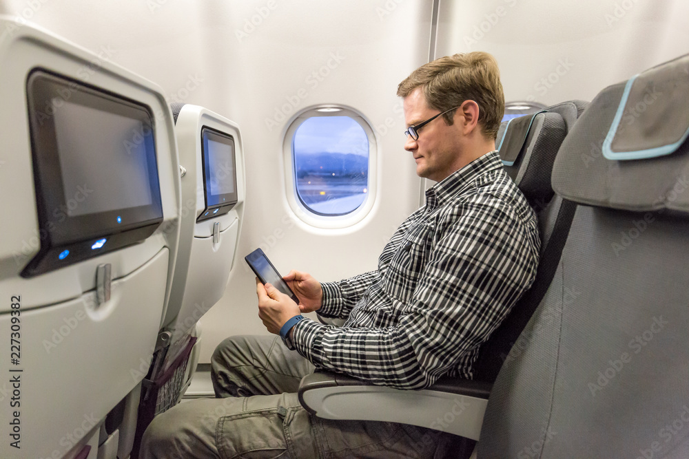 Mann sitzt im Flugzeug in einer leeren Sitzreihe mit seinem eBook-Reader