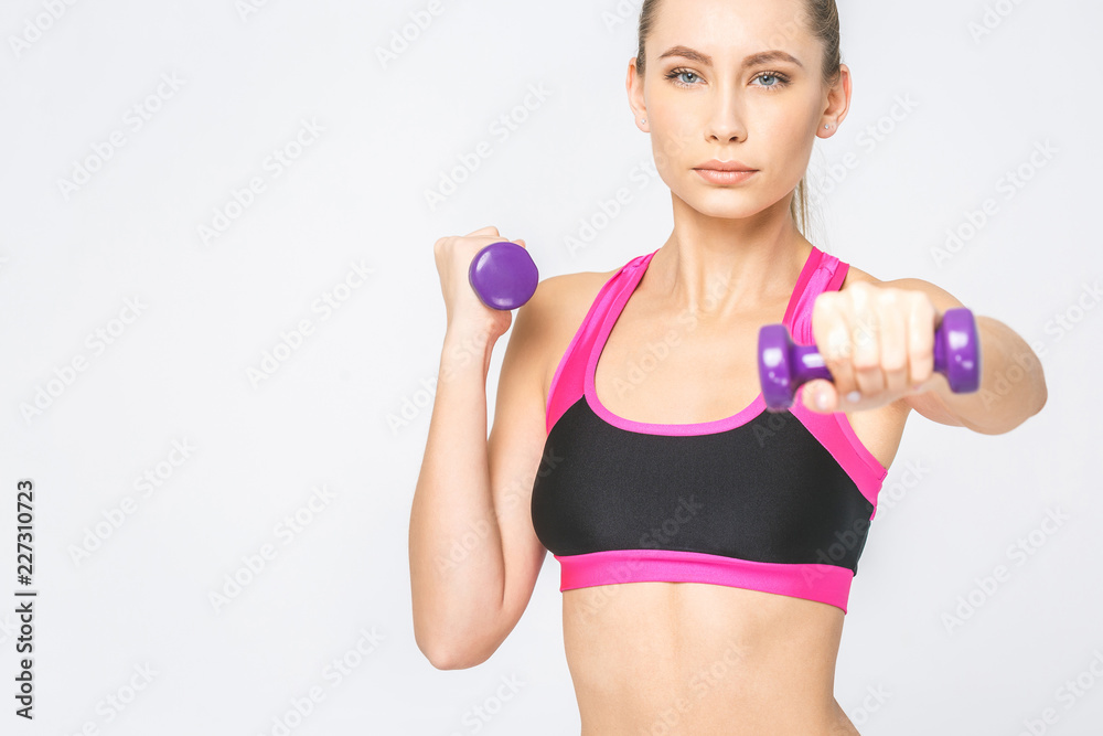 Close-up of concentrated, serious young fitness woman lifting dumbbells smiling and energetic. Isolated over white background. Close-up of concentrated, serious young fitness woman lifting dumbbells smiling and energetic. Isolated over white background.