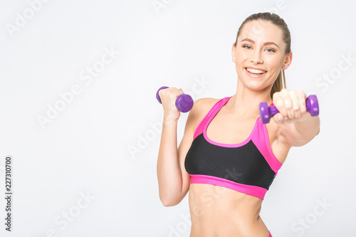Close-uo of happy young fitness woman lifting dumbbells smiling and energetic. Isolated over white background.