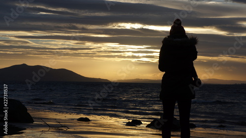 Silhouette of young woman standing looking out at the sea
