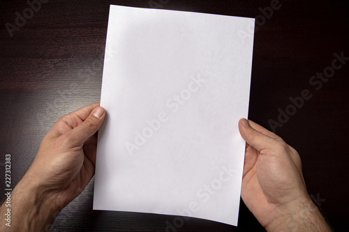 A clean white sheet in the hands is located vertically on a dark background.