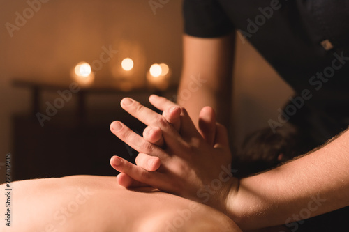 Men's hands make a therapeutic neck massage for a girl lying on a massage couch in a massage spa with dark lighting. Close-up. Dark Key photo