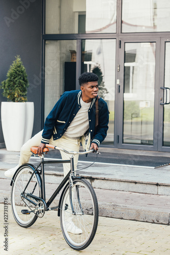 stylish african american man riding bicycle in city