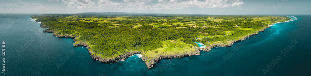 Panorama island, ocean. Aerial drone shot. Indonesia. Spectacular overview of Sumba island the green-capped plain surrounded by the Indian ocean on the blue cloudy sky background.