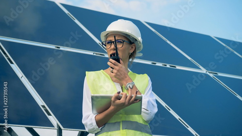 An engineer works with devices, standing on a roof near solar batteries. Alternative, green energy concept.