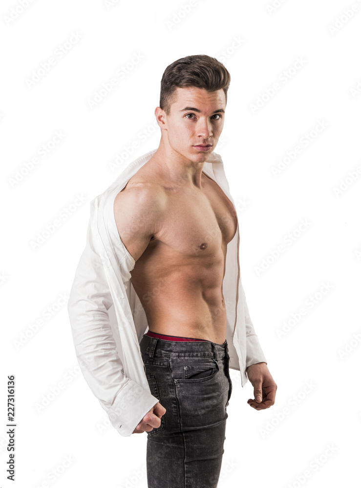 Handsome young muscular man shirtless wearing jeans, taking off white shirt  on naked muscle torso, on light background in studio shot Stock Photo |  Adobe Stock