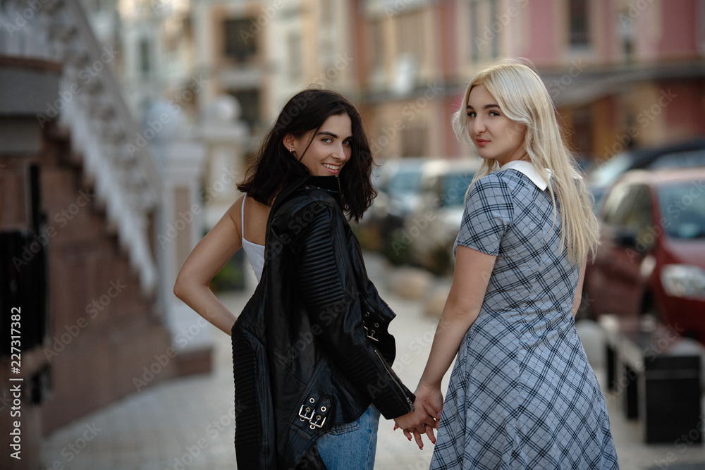 Two young lesbians walking outside. Holding hand in hand. Looking back. Samesex love concept.