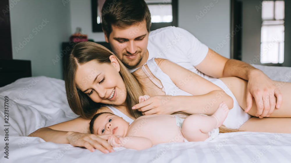 cheerful family laying with adorable little baby son in bed at home cheerful family laying with adorable little baby son in bed at home