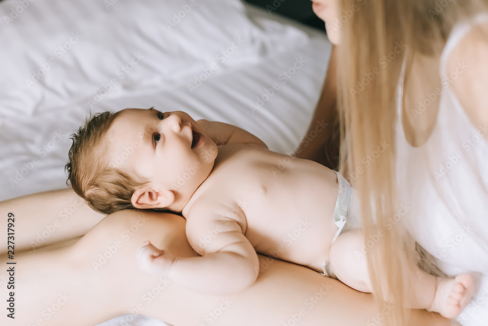 cropped image of mother playing with smiling little baby boy in bed at home
