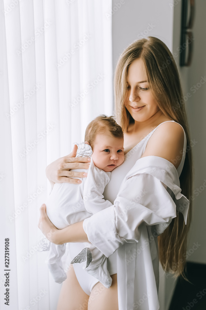 smiling mother carrying little baby boy in front of curtains at home smiling mother carrying little baby boy in front of curtains at home