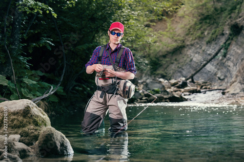 A fisherman chooses bait for trout fishing in the river. Fishing in the creek fly fishing lure. Activity sports fishing wading.
