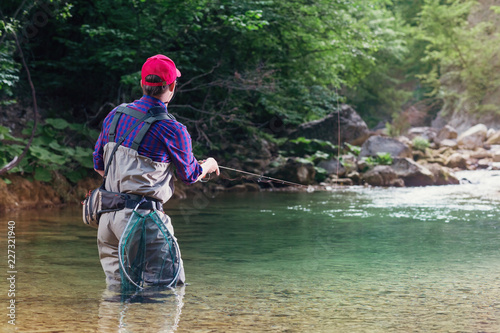 Fisherman catches a fish in the river with fly fishing. Catching trout and bass in the stream. Healthy lifestyle.
